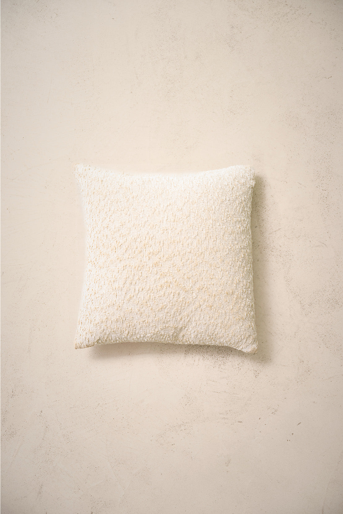 coussin carré CASTLE en bouclé écru à couture simple, sur un mur en enduit crème