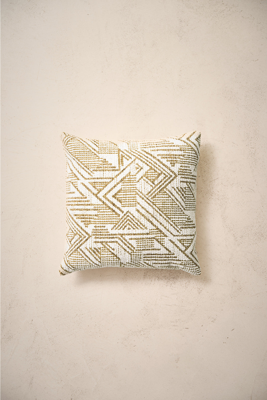 coussin carré CASTLE à motif géométrique écru et marron, sur un mur en enduit crème