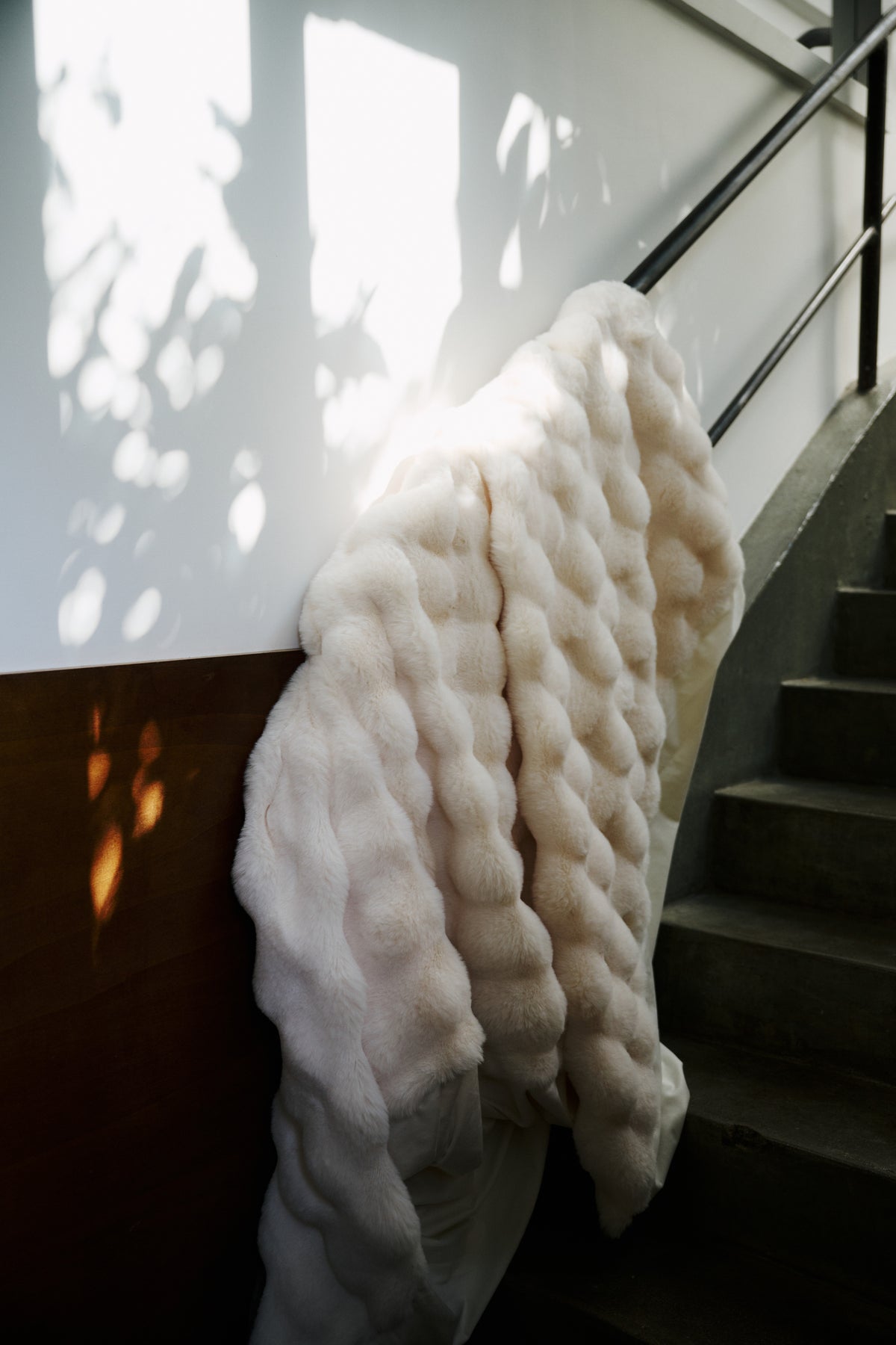 plaid OLYMPE en fausse fourrure écrue posé sur la rampe d'un escalier