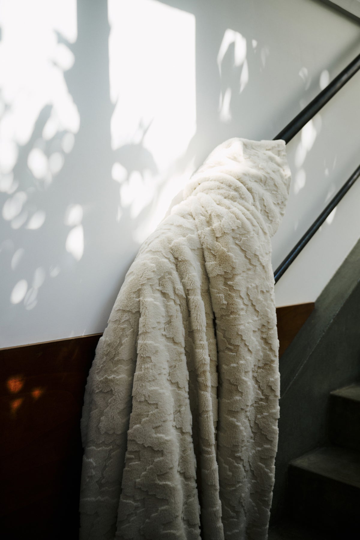 plaid EVEREST en fausse fourrure beige posé sur la rampe d'un escalier, à contre-jour