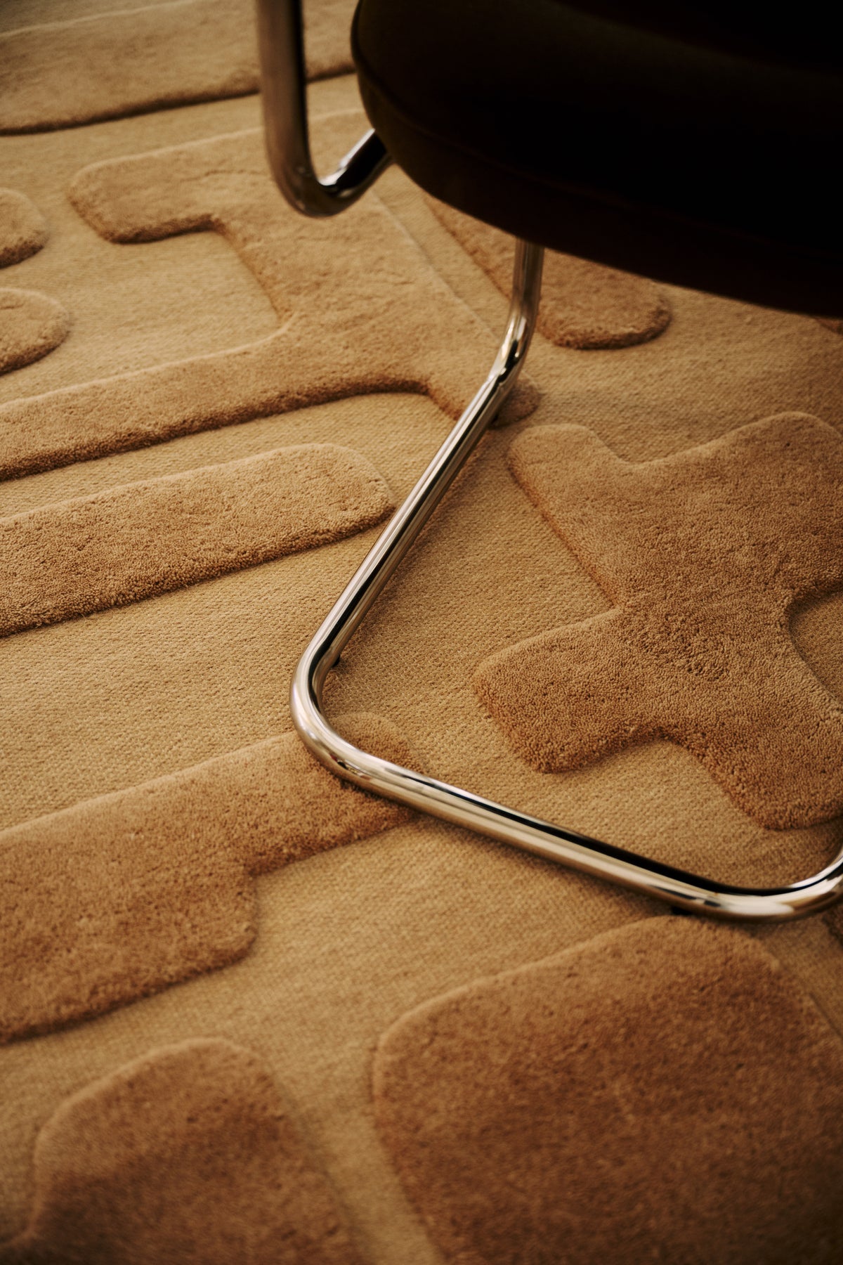 gros plan sur les blocs en relief d'un tapis Maze caramel au pied d'une chaise chromée