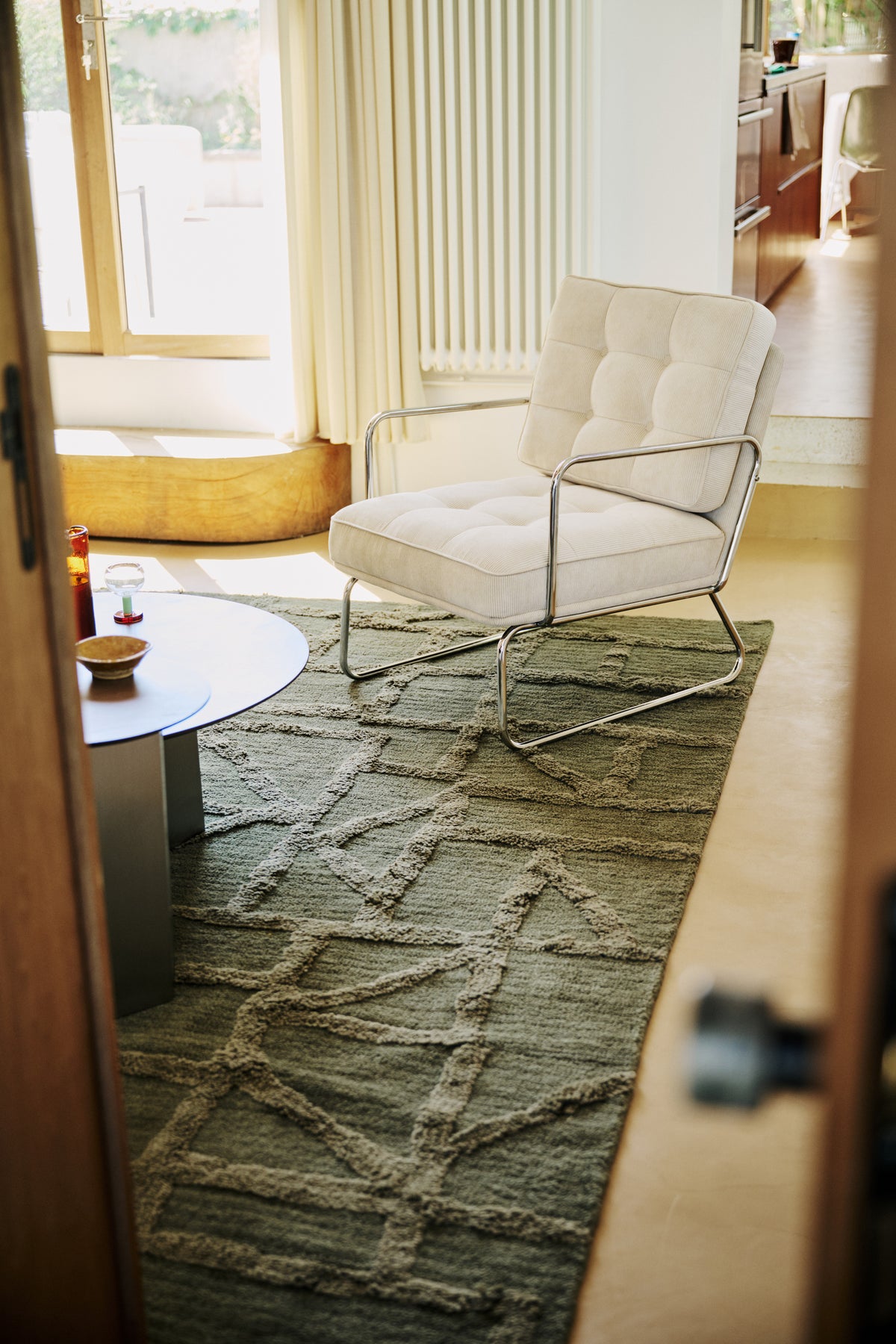 salon avec tapis Strato vert kaki, fauteuil côtelé écru et table basse ronde en métal