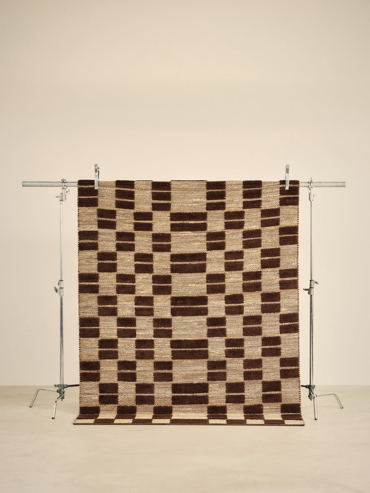 tapis de salon Saxton en jute et laine brune à damier suspendu sur un portant de studio