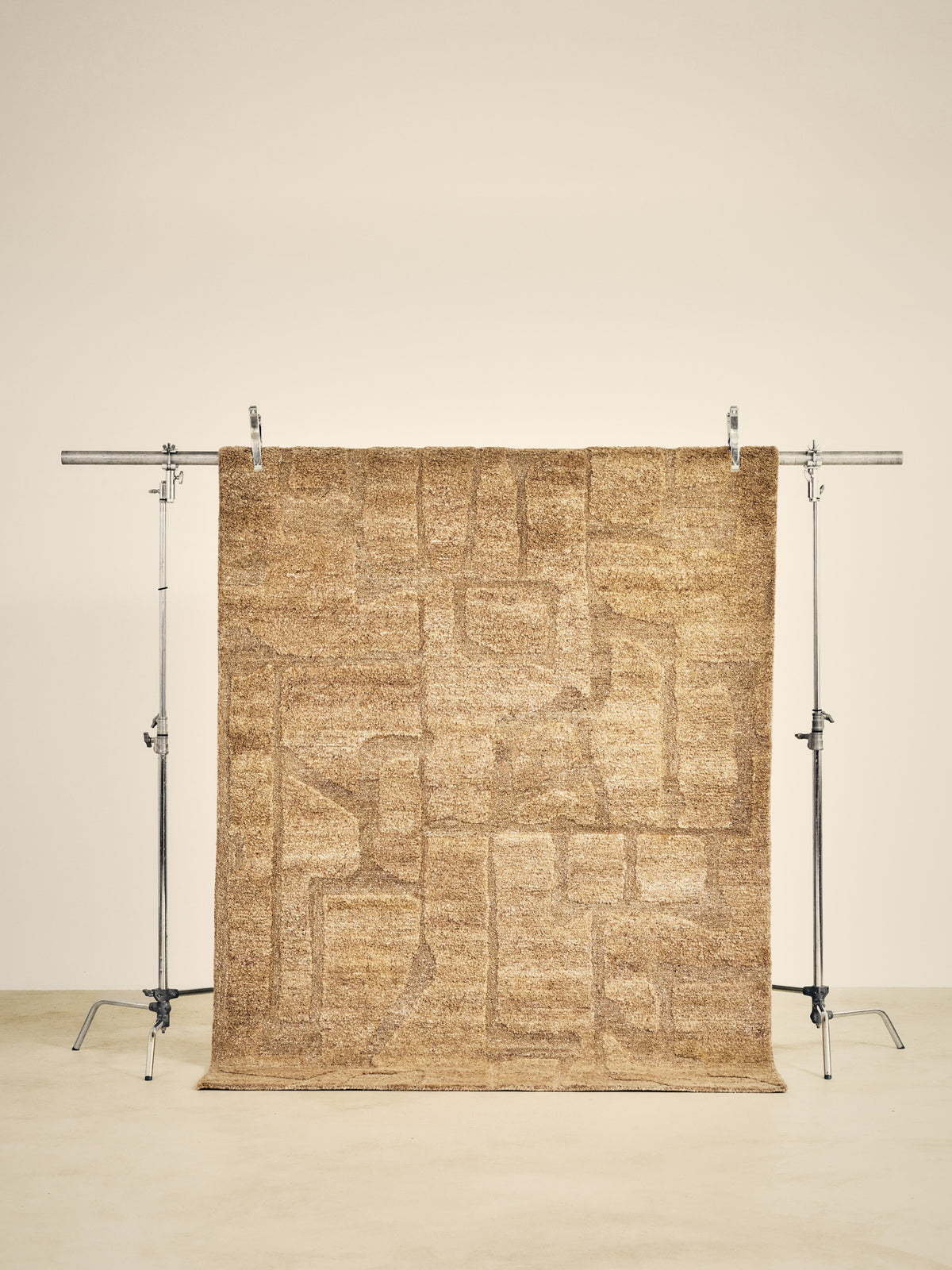 tapis de salon Shard beige chiné à poils longs suspendu sur un portant de studio