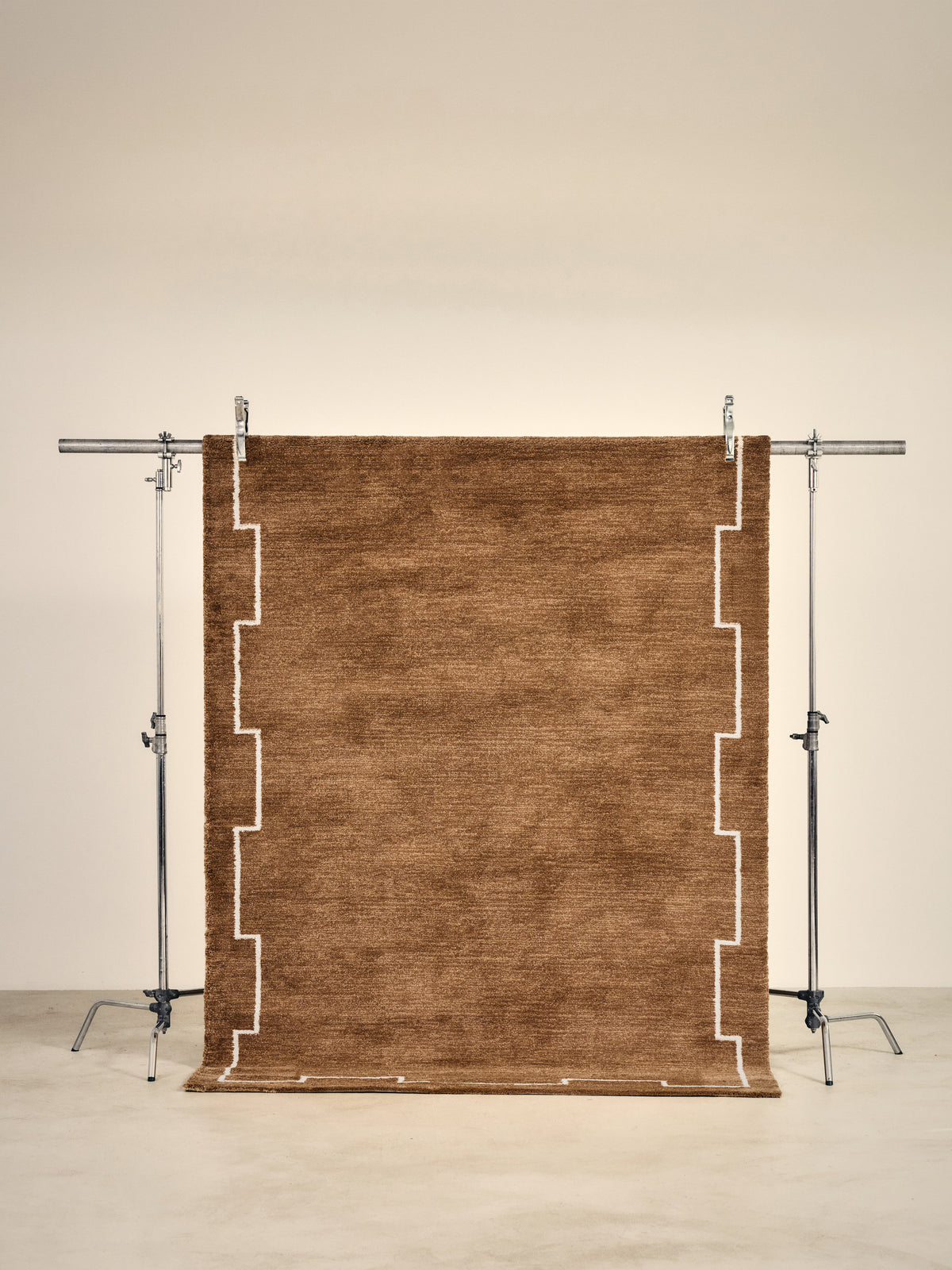 tapis de salon Crest terracotta à motif à créneaux écru suspendu sur un portant de studio