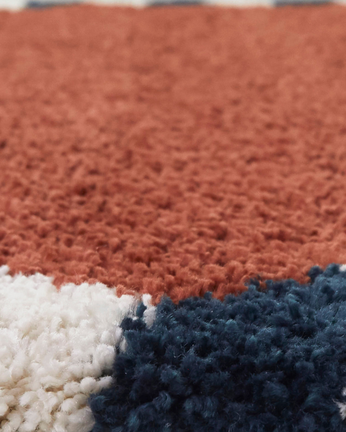 gros plan sur le velours terracotta et l'amorce de la bordure écrue d'un tapis Ardmore