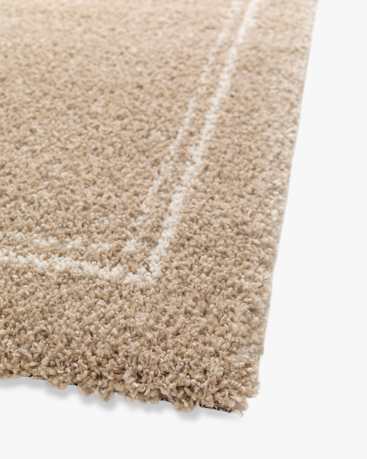 gros plan sur l'angle du double liseré écru sur le velours beige d'un tapis Estero