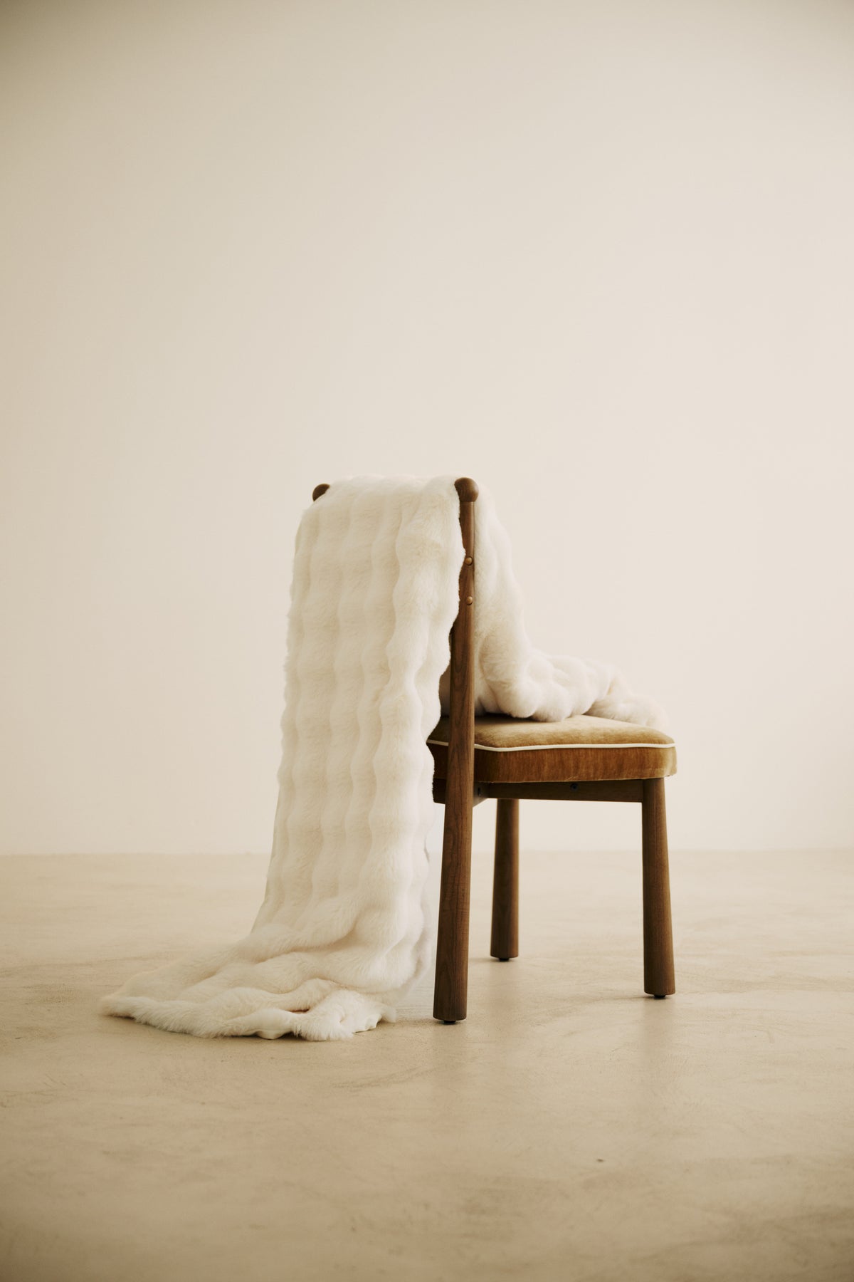 plaid OLYMPE en fausse fourrure écrue à reliefs ondulés, drapé sur une chaise en bois