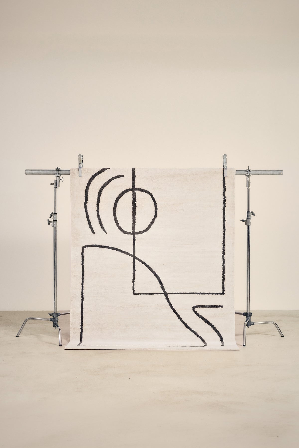 tapis ARCA petit format, écru à tracés noirs abstraits, suspendu sur un portant de studio
