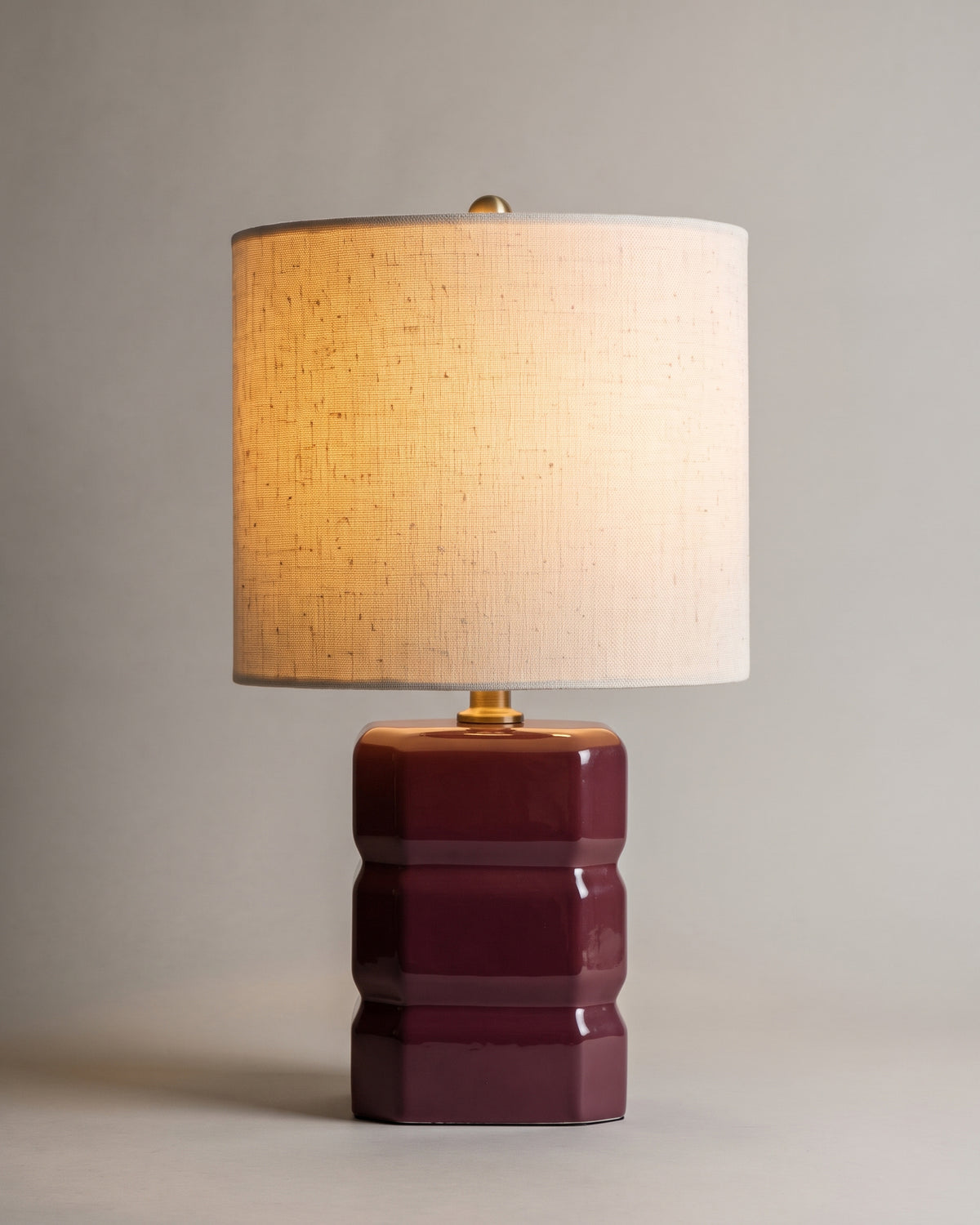 lampe de table ANYA allumée, pied en céramique prune à gradins et abat-jour en lin écru