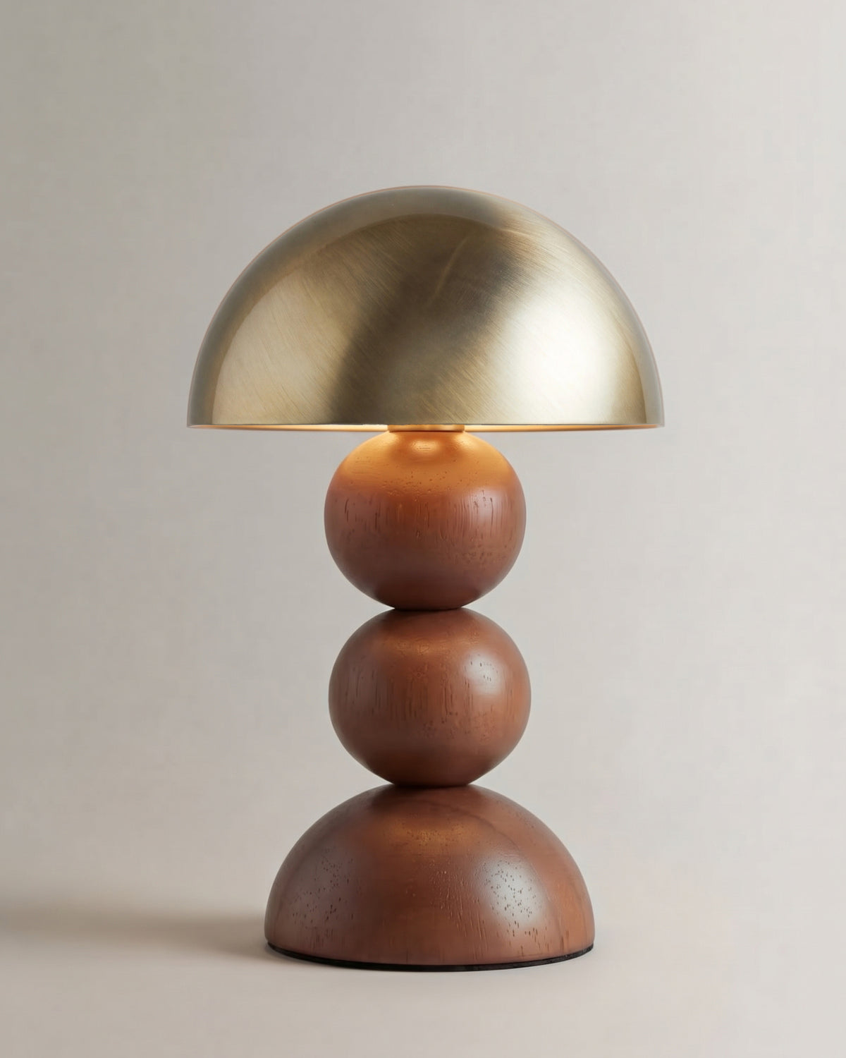 lampe de table GIGI allumée, dôme en laiton brossé sur un pied en sphères de noyer
