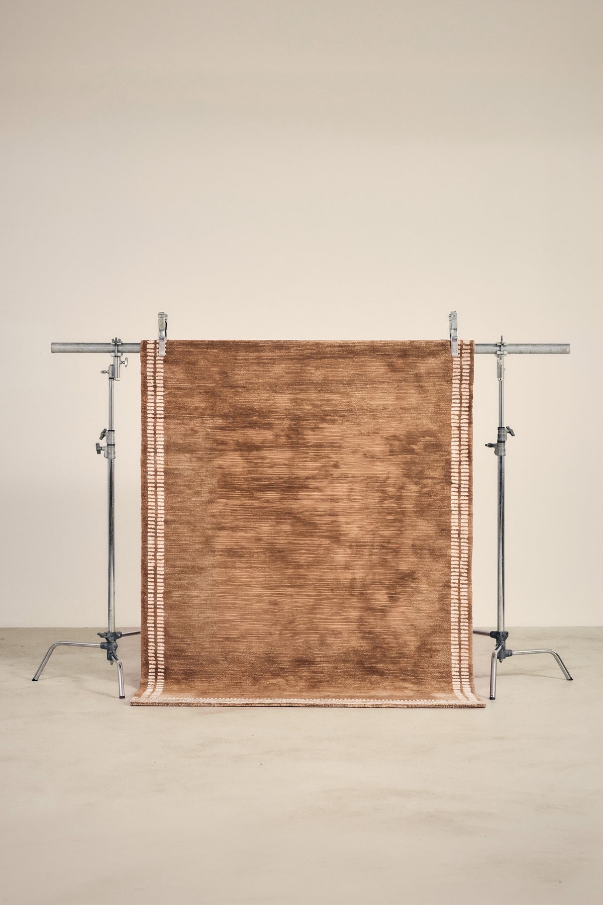 tapis HAVEN terracotta chiné bordé de bandes écrues tiretées, sur un portant de studio
