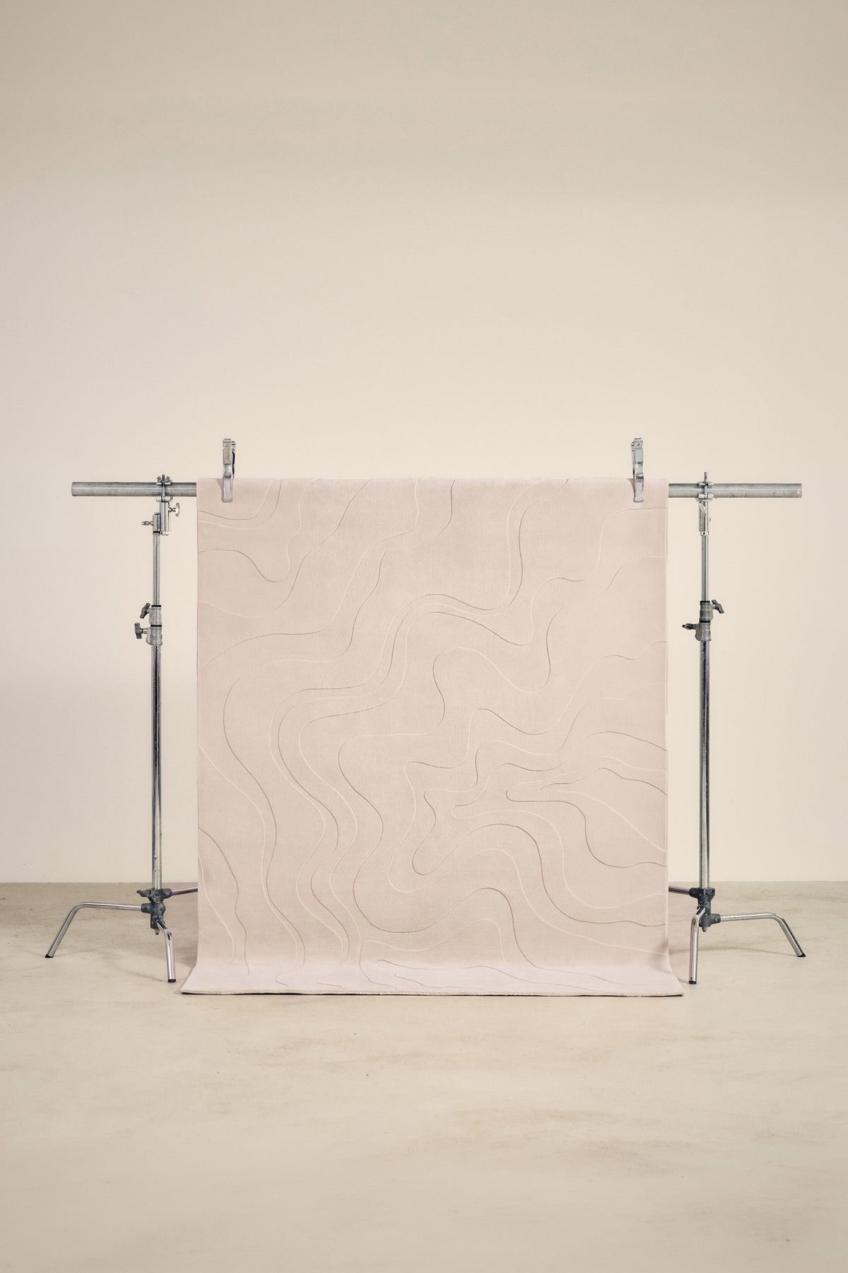 tapis design Ikat écru à lignes ondulantes en relief suspendu sur un portant de studio