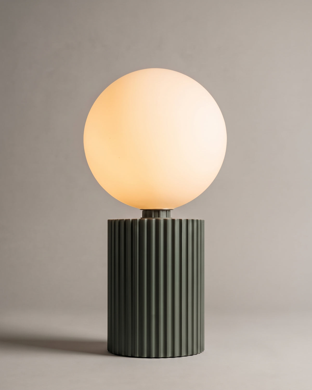 lampe de table LUNA allumée, globe en verre opalin sur un socle cannelé vert kaki