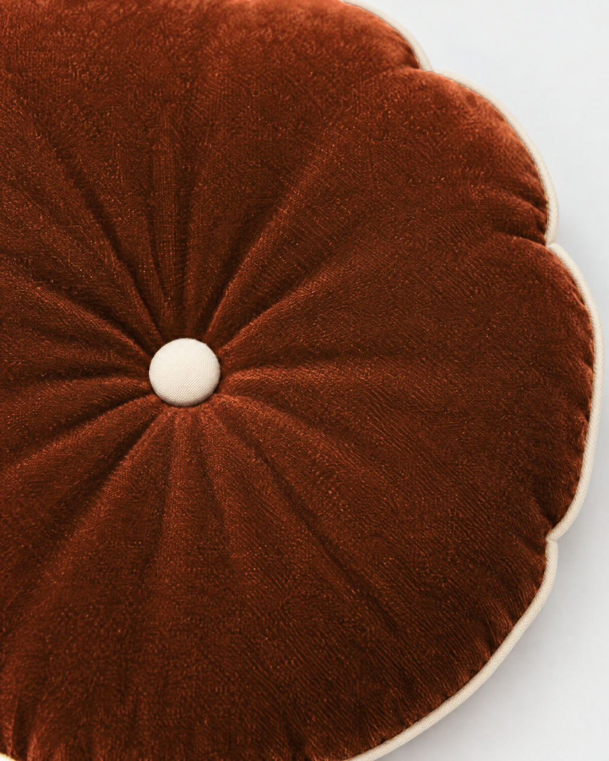 gros plan sur le bouton écru du coussin rond MOON et les plis rayonnants du velours cognac