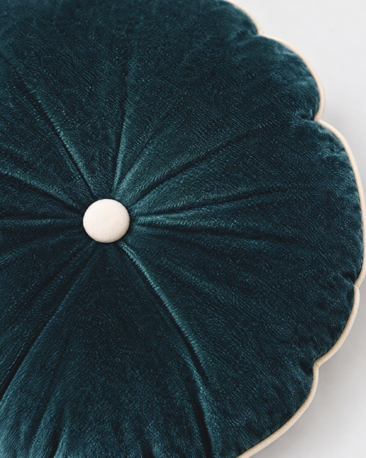 gros plan sur le bouton écru du coussin rond MOON et les plis rayonnants du velours bleu canard