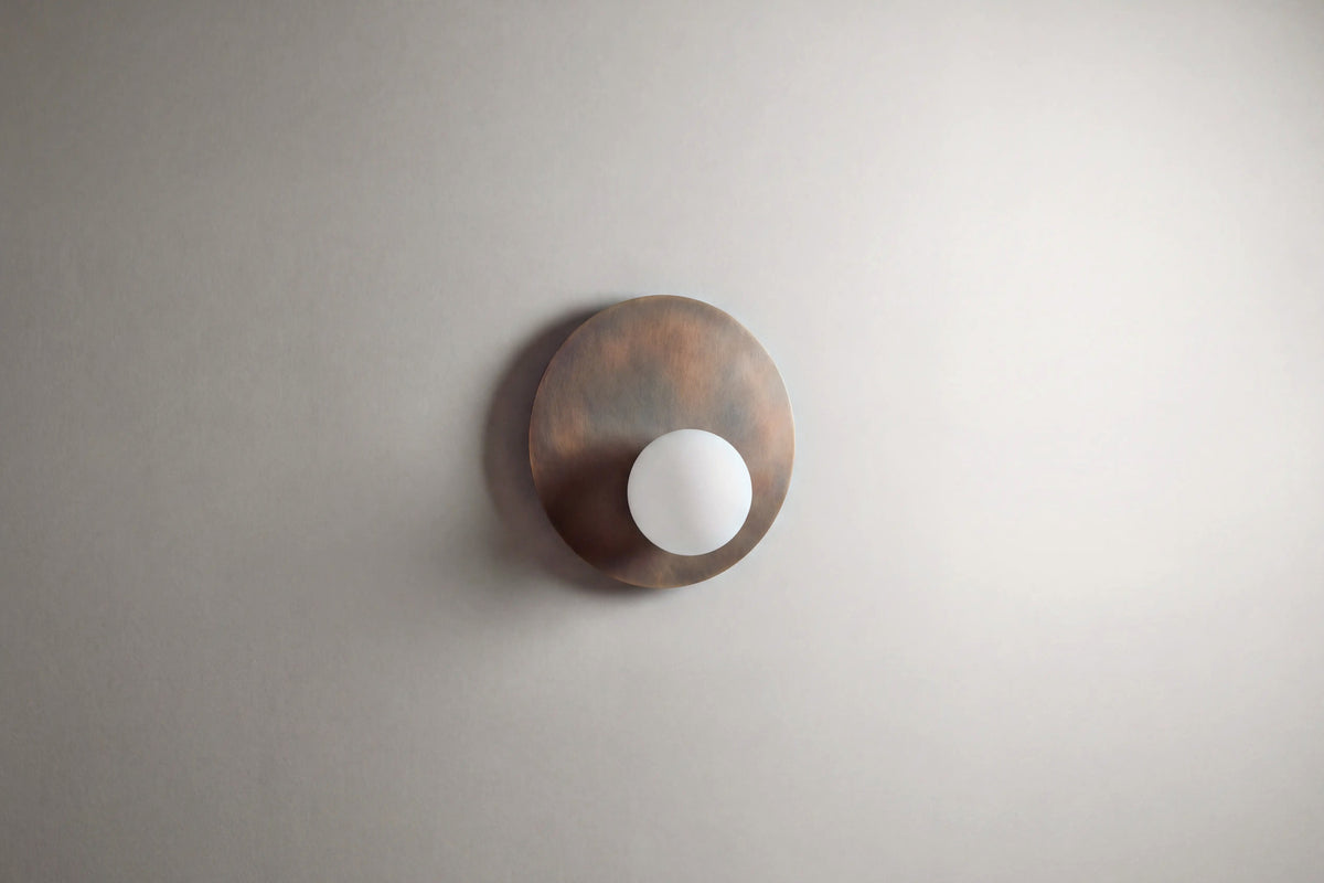 applique murale OLUWA en métal bronze patiné et globe opalin, éteinte sur un mur clair