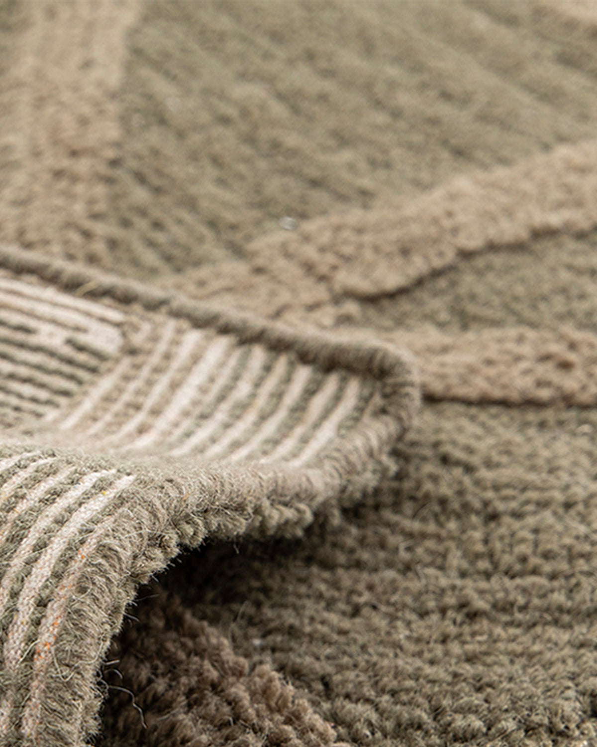 gros plan sur l'envers tissé et la lisière surjetée d'un tapis de salon Strato vert kaki