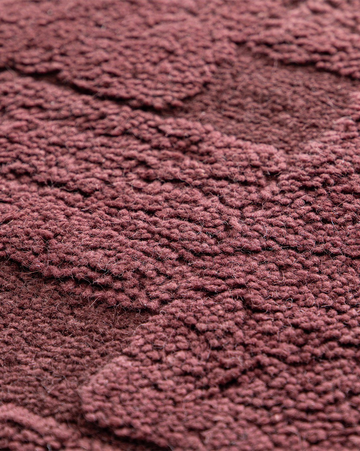 gros plan sur les blocs entrelacés en relief d'un tapis de salon Woven bordeaux ton sur ton
