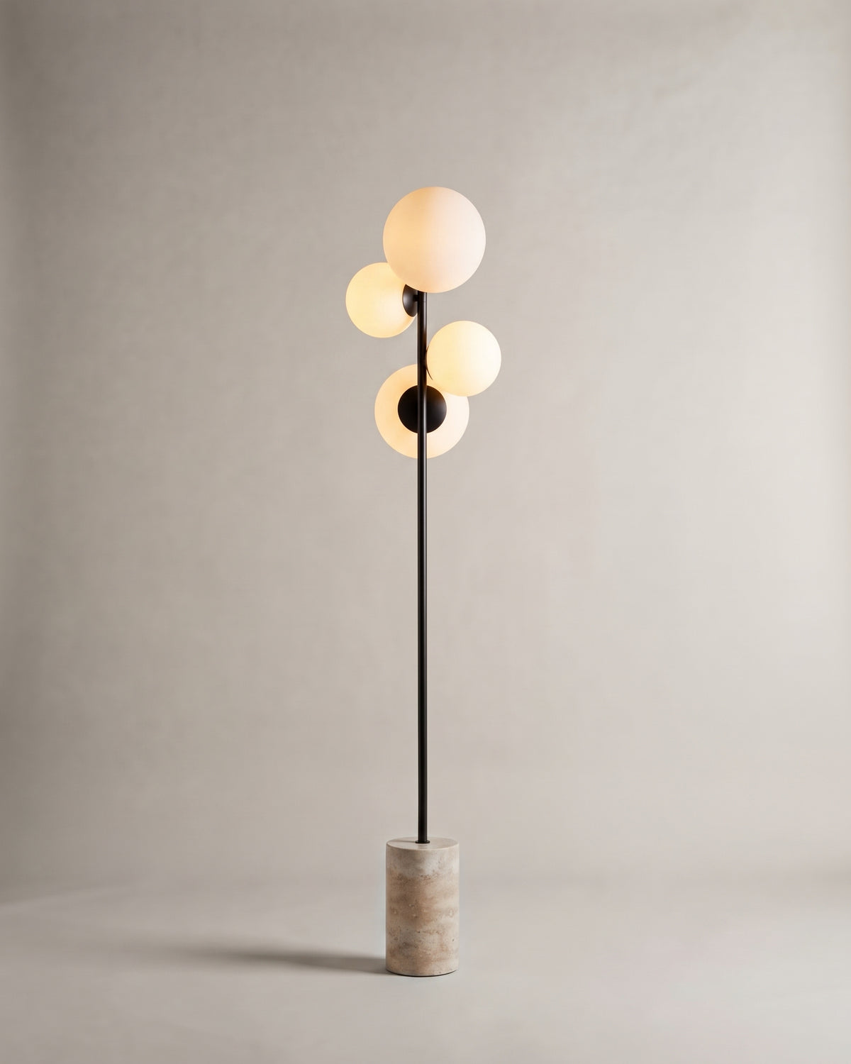 lampadaire SKULL allumé, quatre globes opalins sur tige noire et base en travertin