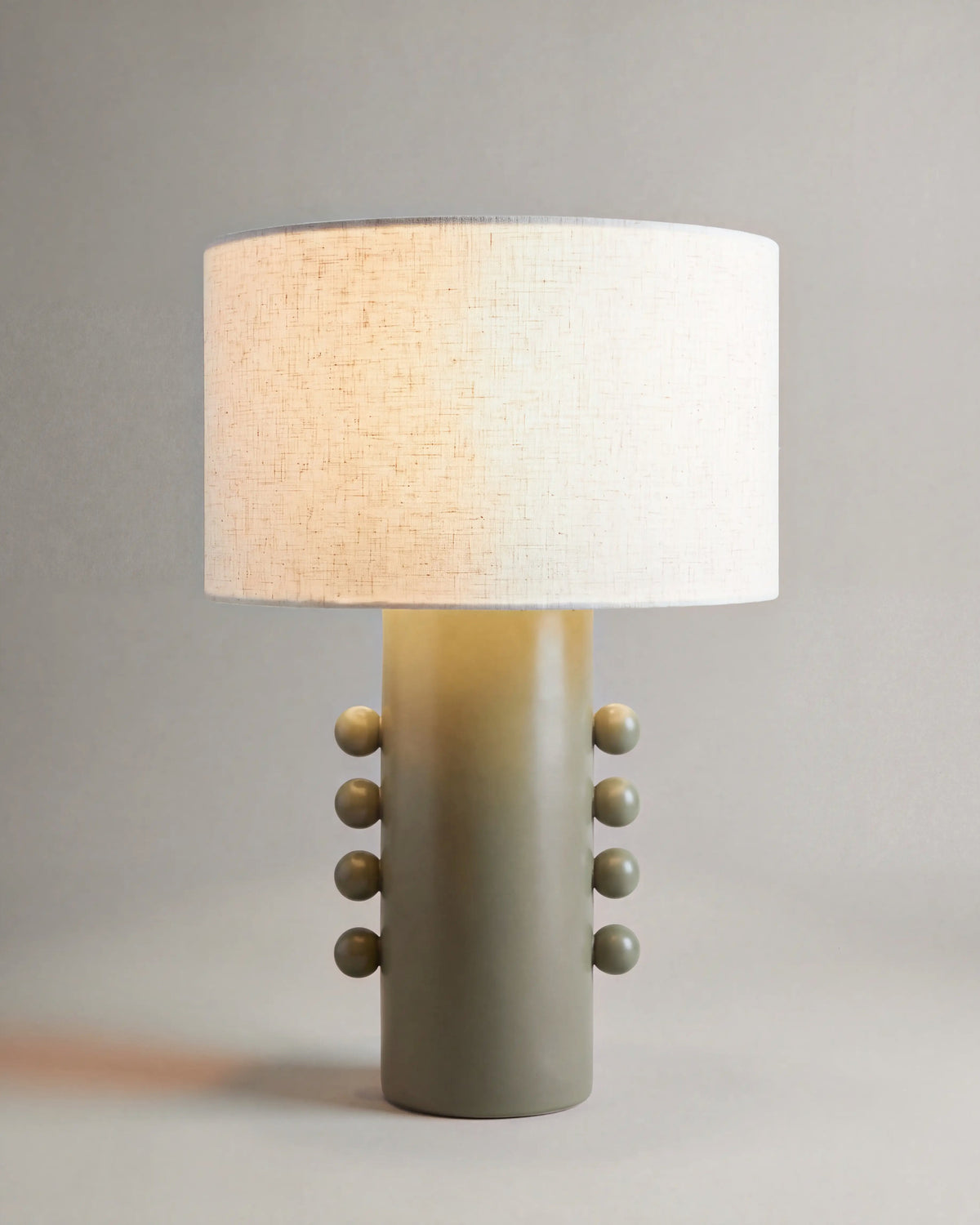 lampe de table SOLI allumée, pied en céramique vert kaki à sphères et abat-jour écru